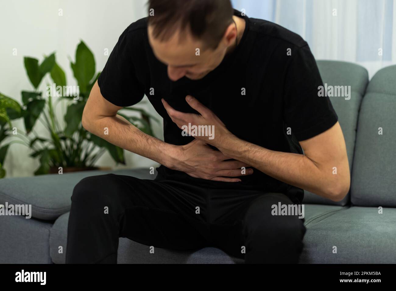 Man suffering with severe stomach pain sitting at home. Hand of mature ...