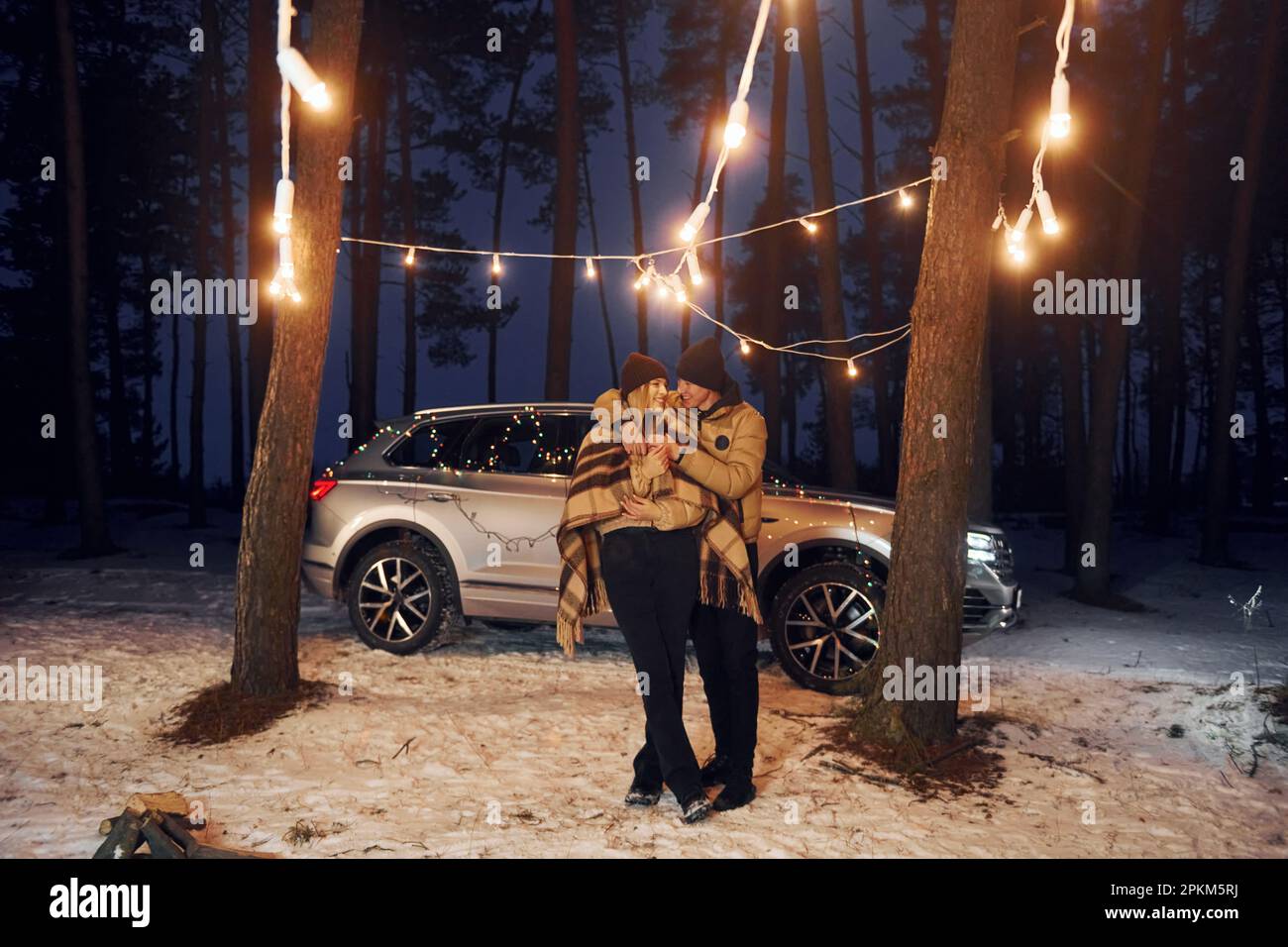 Car is at background. Couple standing in the forest and celebrating New year. Stock Photo
