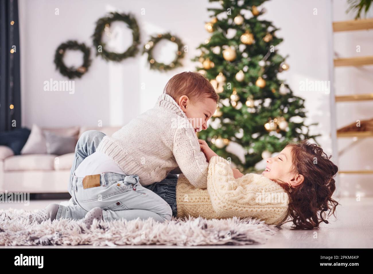 Laying down and playing. Little brother and sister is at christmas decorated room together. Stock Photo