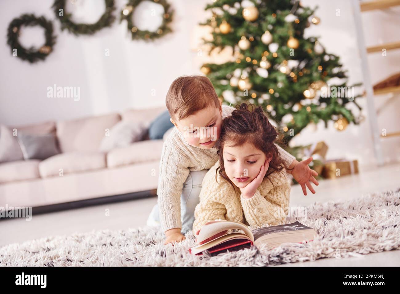 Laying down on the ground. Little brother and sister is at christmas decorated room together. Stock Photo