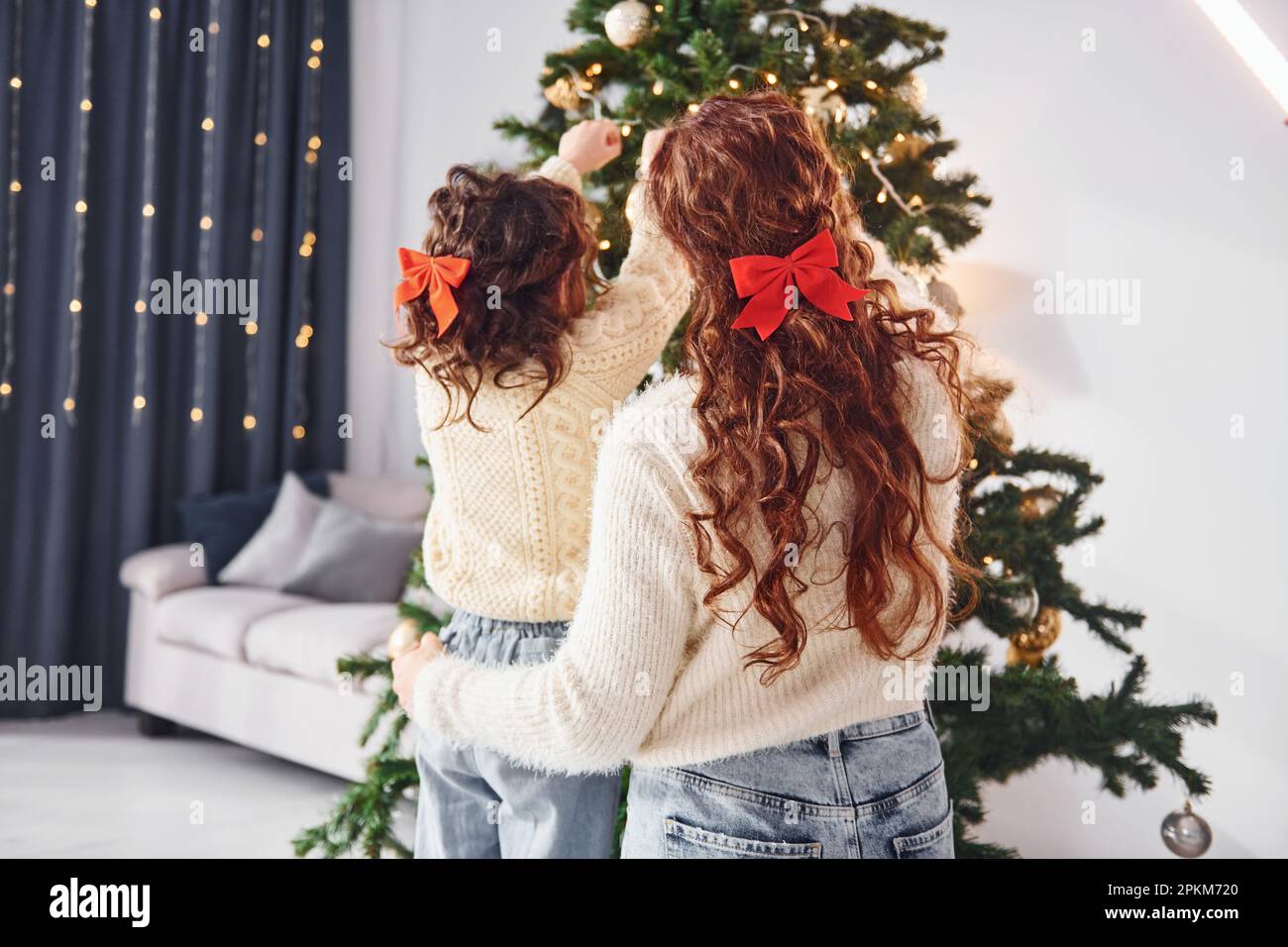 Rear view. Mother with her little daughter is at home. Christmas decorations. Stock Photo