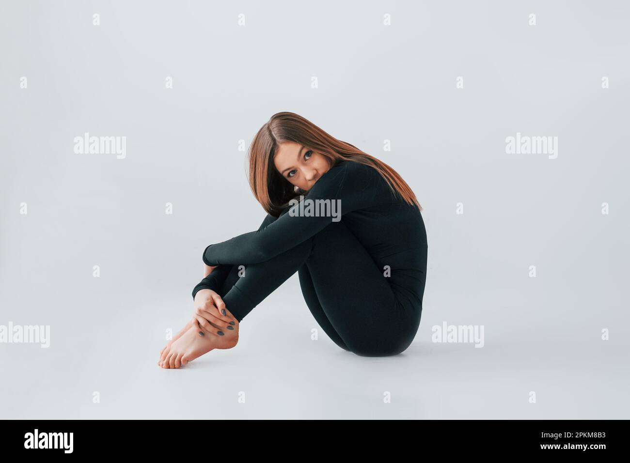 On the floor. Young woman in sportive clothes doing gymnastics indoors. Stock Photo