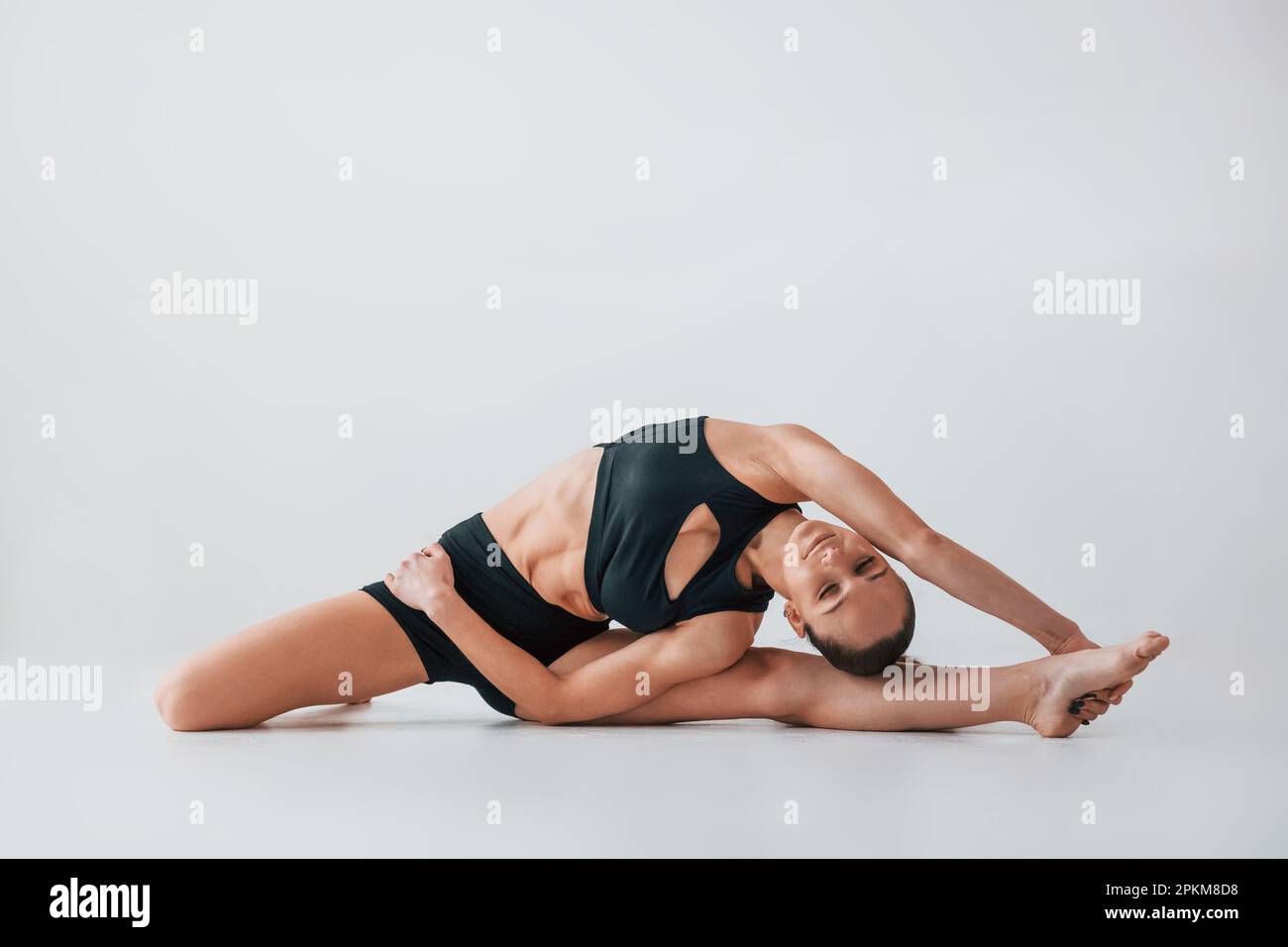 Stretching to the side. Young woman in sportive clothes doing gymnastics indoors. Stock Photo