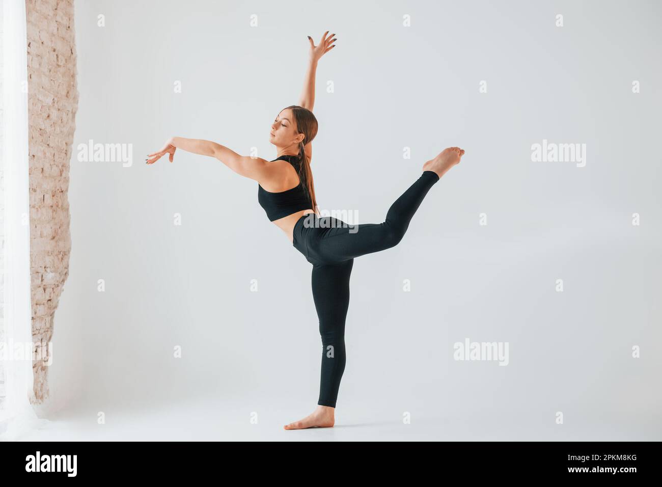 In the studio against white background. Young woman in sportive clothes doing gymnastics indoors. Stock Photo