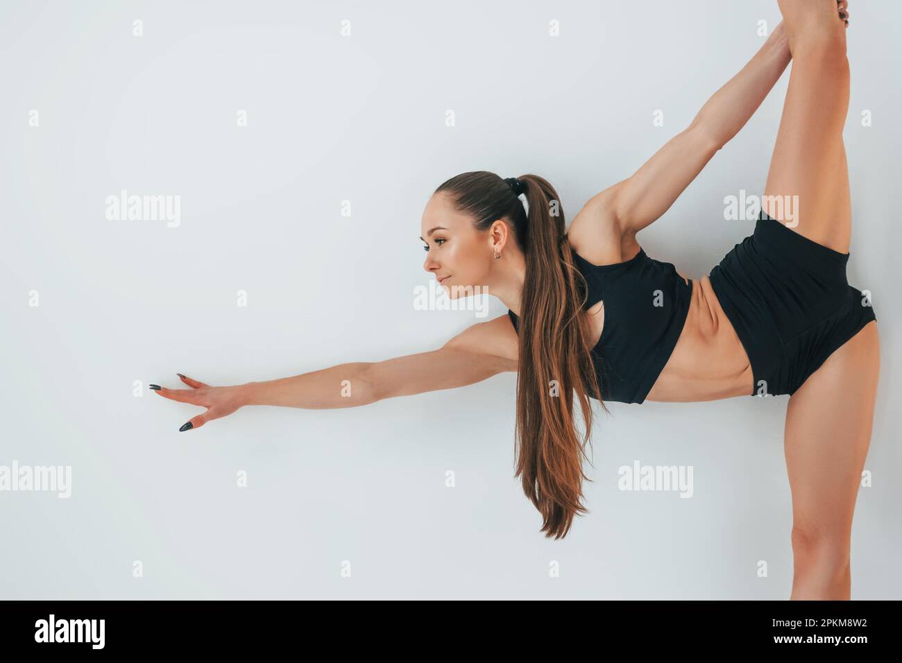 Standing against white background. Young woman in sportive clothes doing gymnastics indoors. Stock Photo