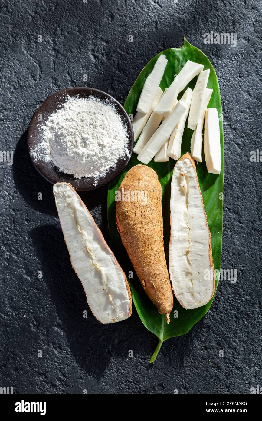 pile of cassava fruit and cassava flour on a background of rustic and dark texture (Manihot esculenta) Stock Photo