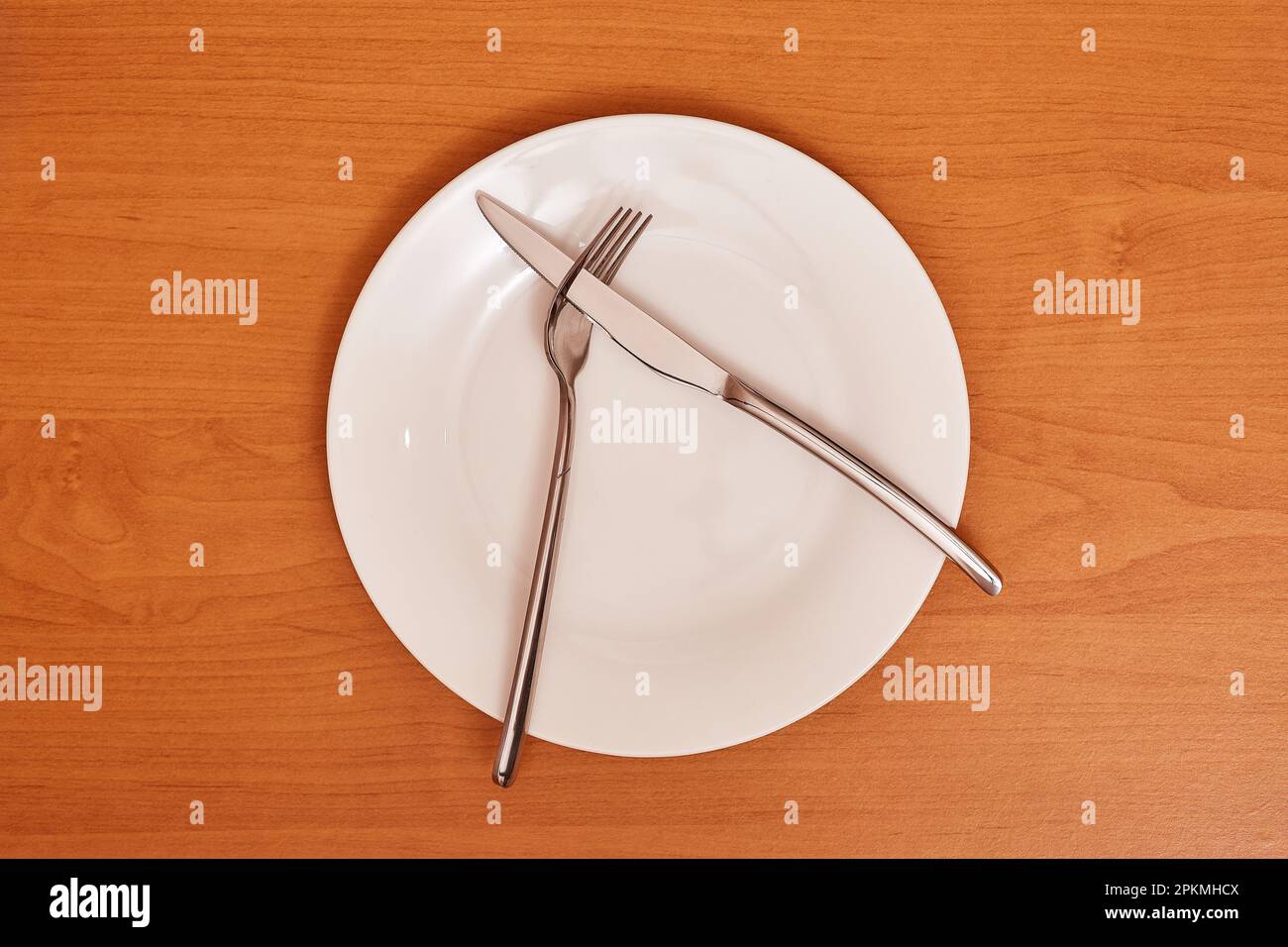 A signal 'Didn't like the dish'. Empty and clean blue plate with fork and knife on a wooden table as an example of table etiquette Stock Photo