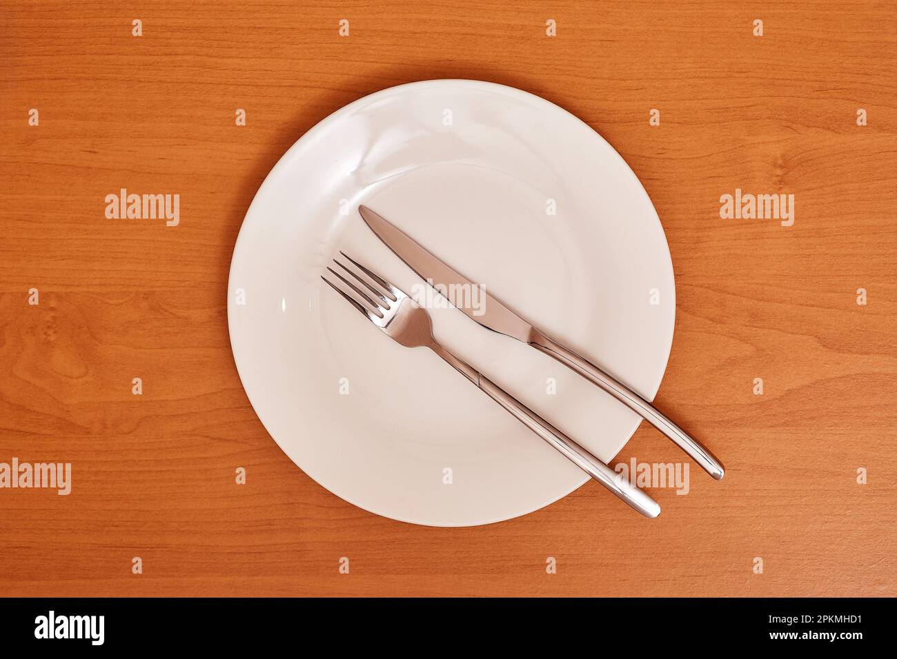 A signal 'The meal was hearty and there was plenty of it'. Empty and clean blue plate with fork and knife on a wooden table as an example of table eti Stock Photo