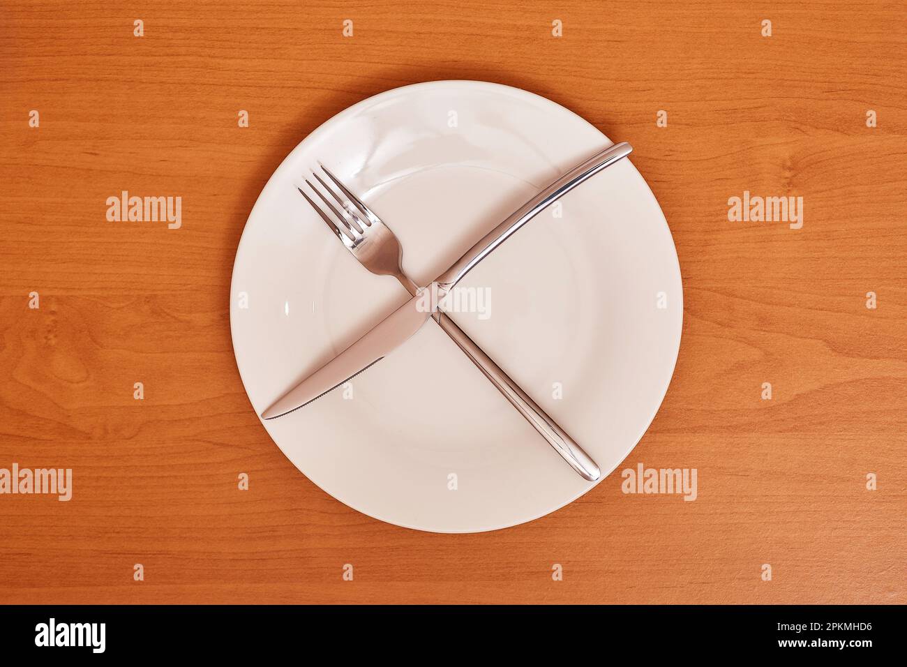 A signal 'Meal break'. Empty and clean blue plate with fork and knife on a wooden table as an example of table etiquette Stock Photo