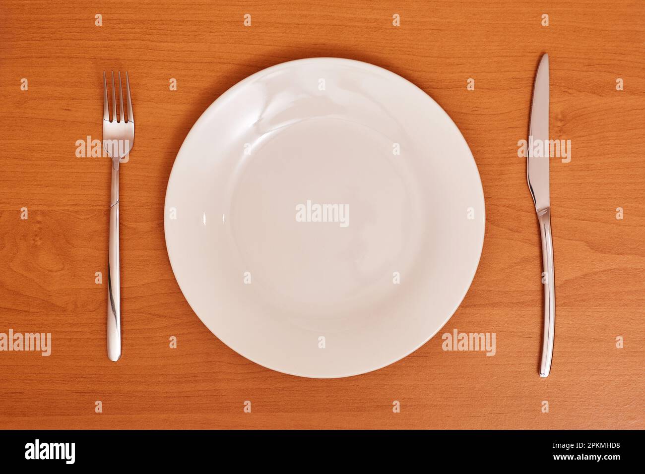 Empty and clean blue plate with fork and knife on a wooden table as an example of table etiquette Stock Photo