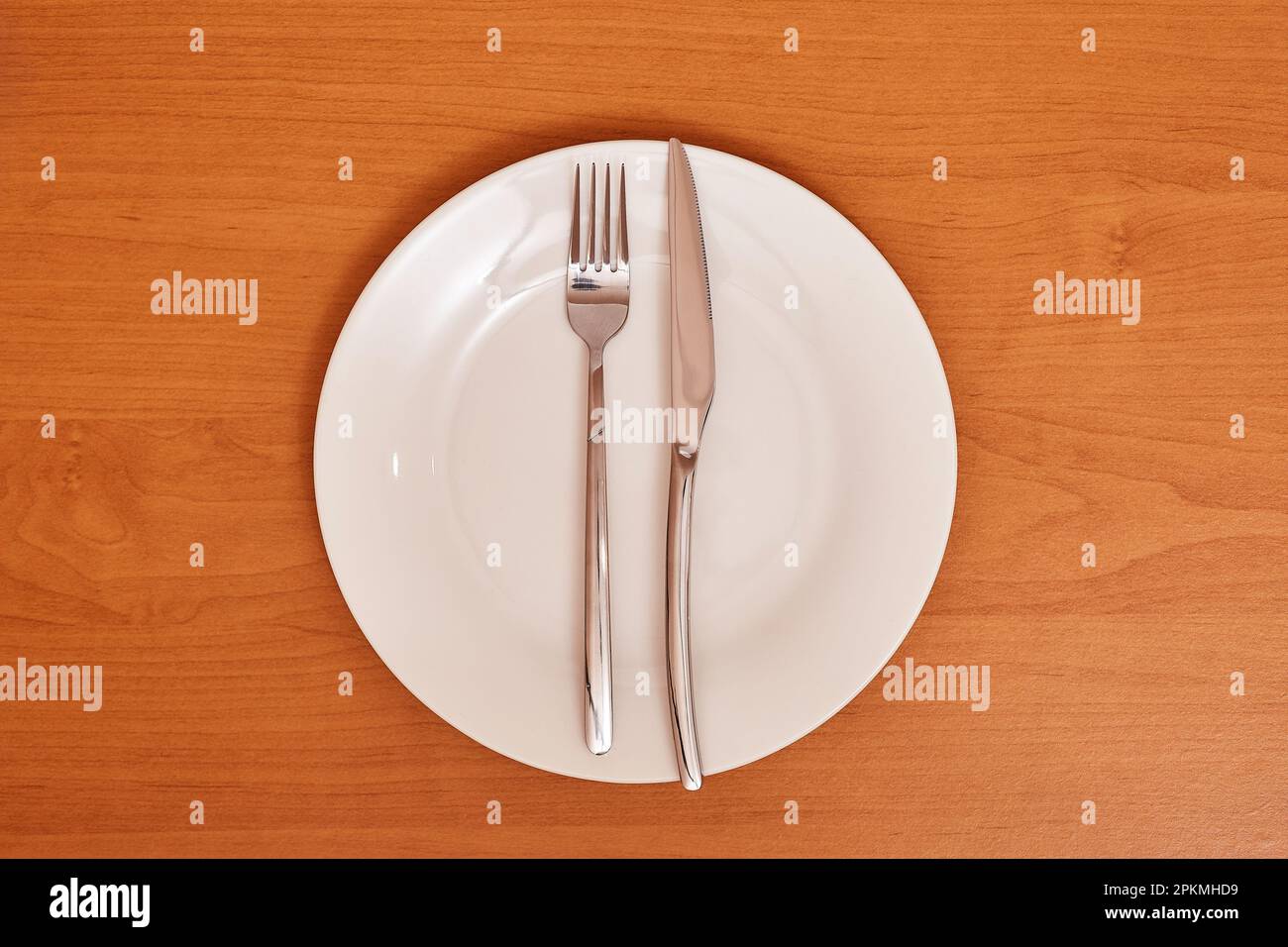 A signal 'The dish is wonderful'. Empty and clean blue plate with fork and knife on a wooden table as an example of table etiquette Stock Photo