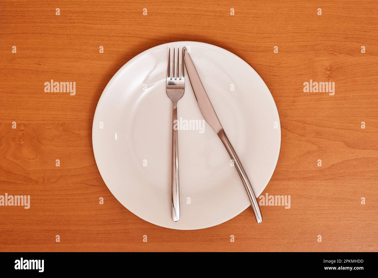 A signal 'There is little food'. Empty and clean blue plate with fork and knife on a wooden table as an example of table etiquette Stock Photo