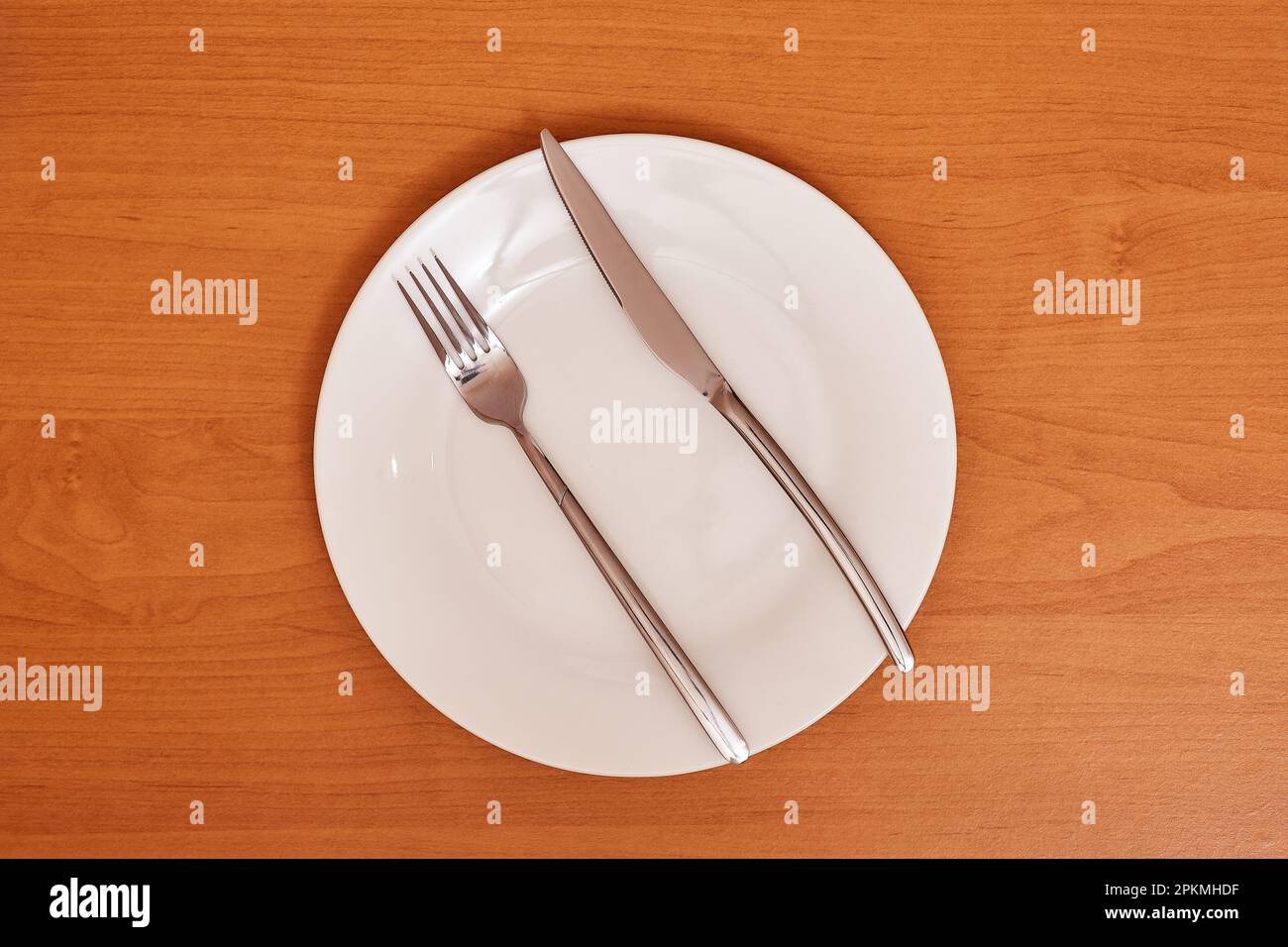 A signal 'The meal was hearty and there was plenty of it'. Empty and clean blue plate with fork and knife on a wooden table as an example of table eti Stock Photo