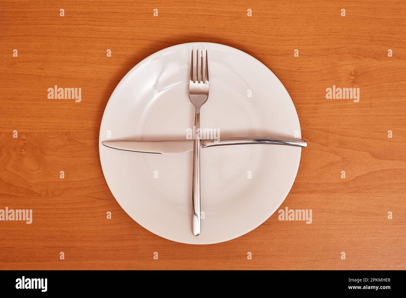 A signal 'I'm waiting for the next meal'. Empty and clean blue plate with fork and knife on a wooden table as an example of table etiquette Stock Photo