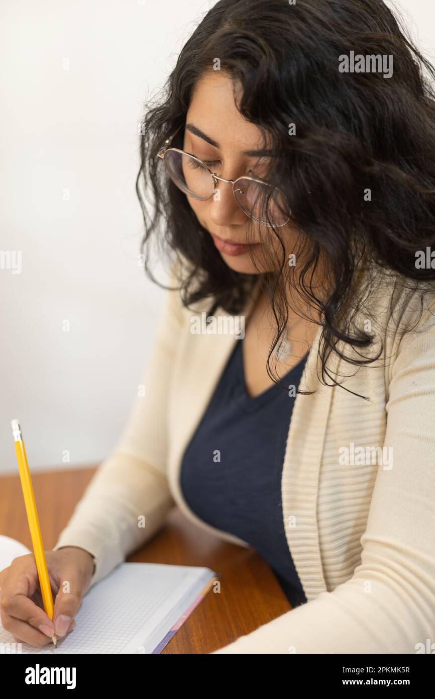 working young latin woman with glasses and short hair, writing with a pencil on a sheet, workplace, creative professional lifestyle, studying Stock Photo