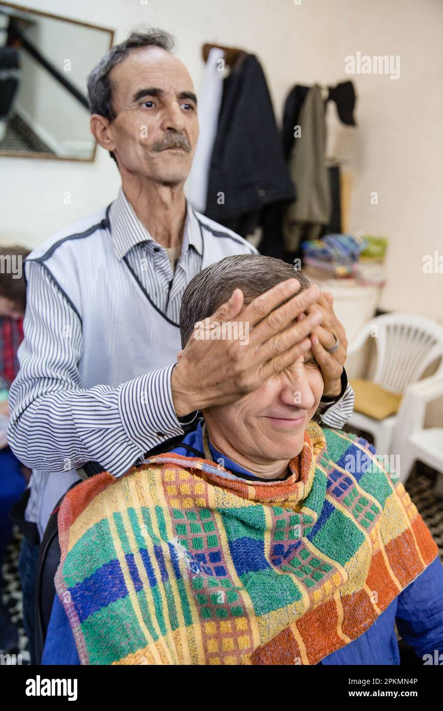An American tourist getting a straight razor shave and a haircut in a barbershop in Marrakech Morocco Stock Photo