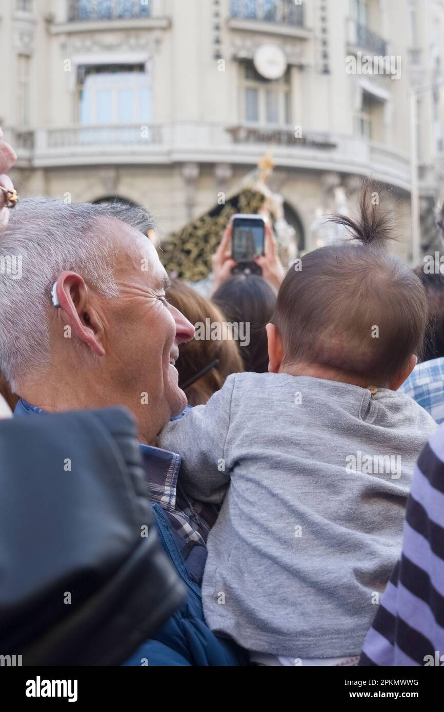 A grandad holding his baby grandaughter to see the procession.  The procession of Jesus of Medinaceli, that leaves from the Basilica by the same name, Stock Photo
