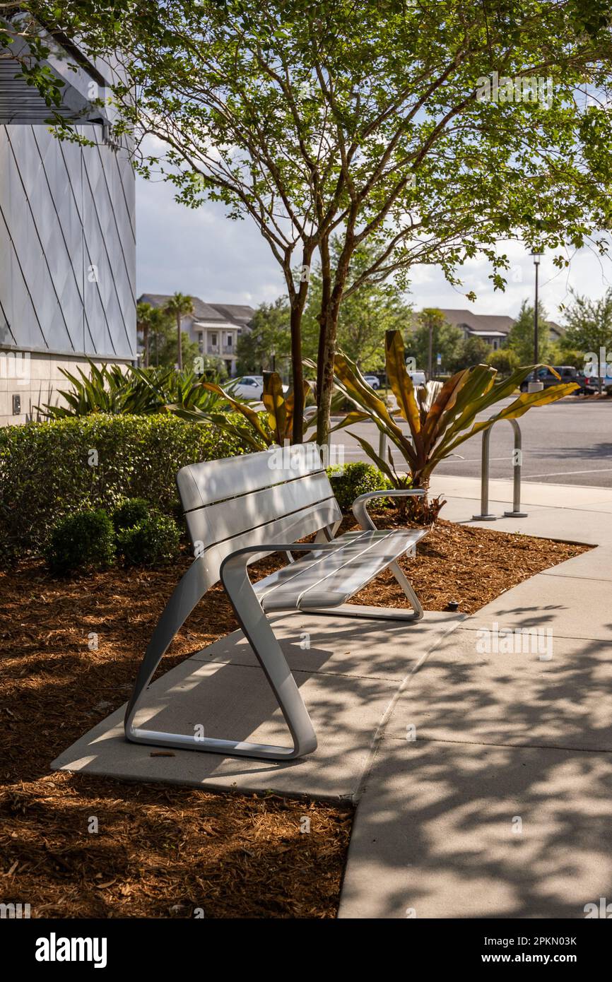 Modern-design bench in the recreational area of Lake Nona, Orlando, Florida. The bench is in the shadow of the trees, sunny day. Stock Photo