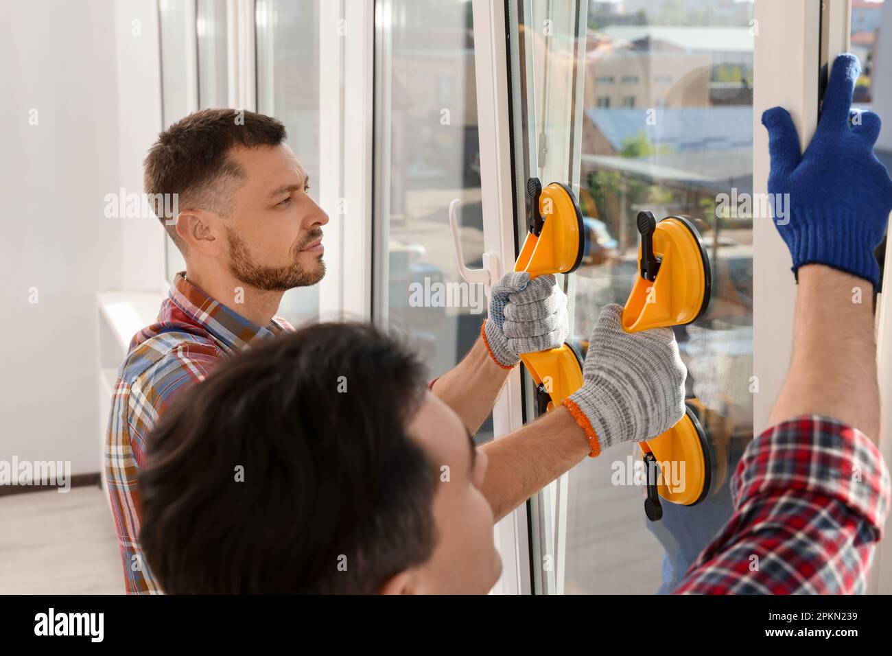 Workers using suction lifters during plastic window installation indoors Stock Photo