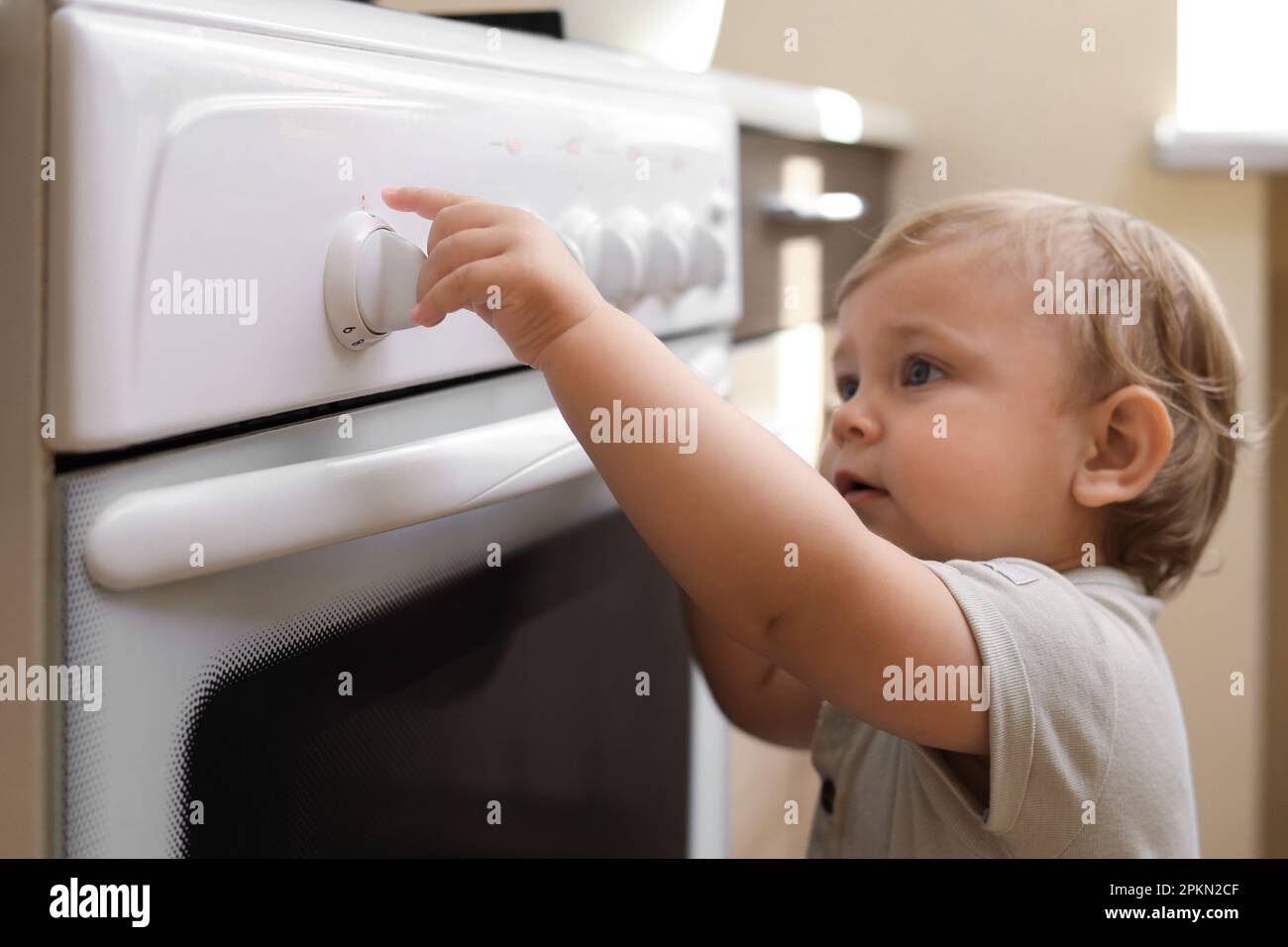 Little child playing with gas stove indoors. Dangers in kitchen Stock