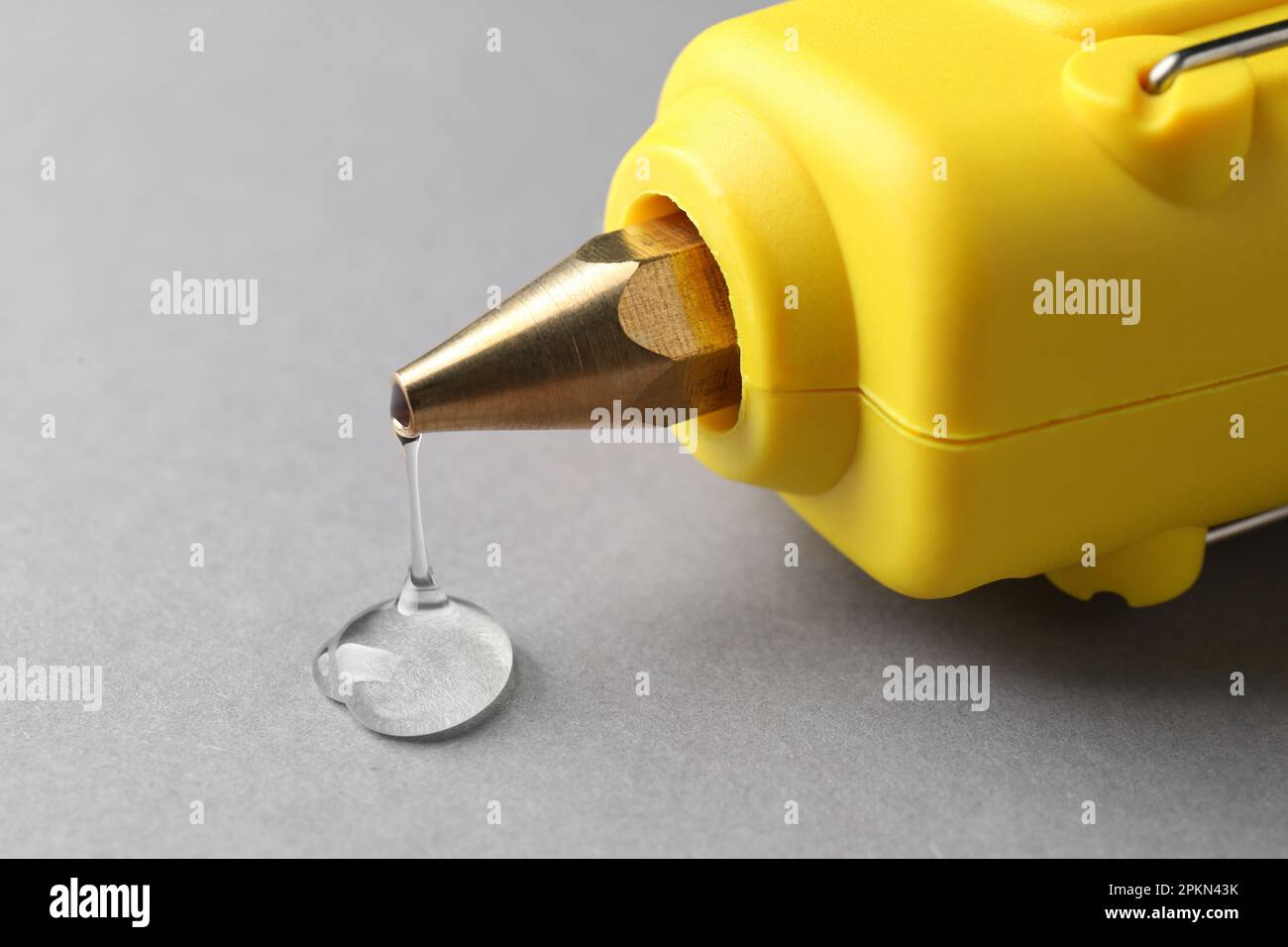 Melted glue dripping out of hot gun nozzle on grey background, closeup