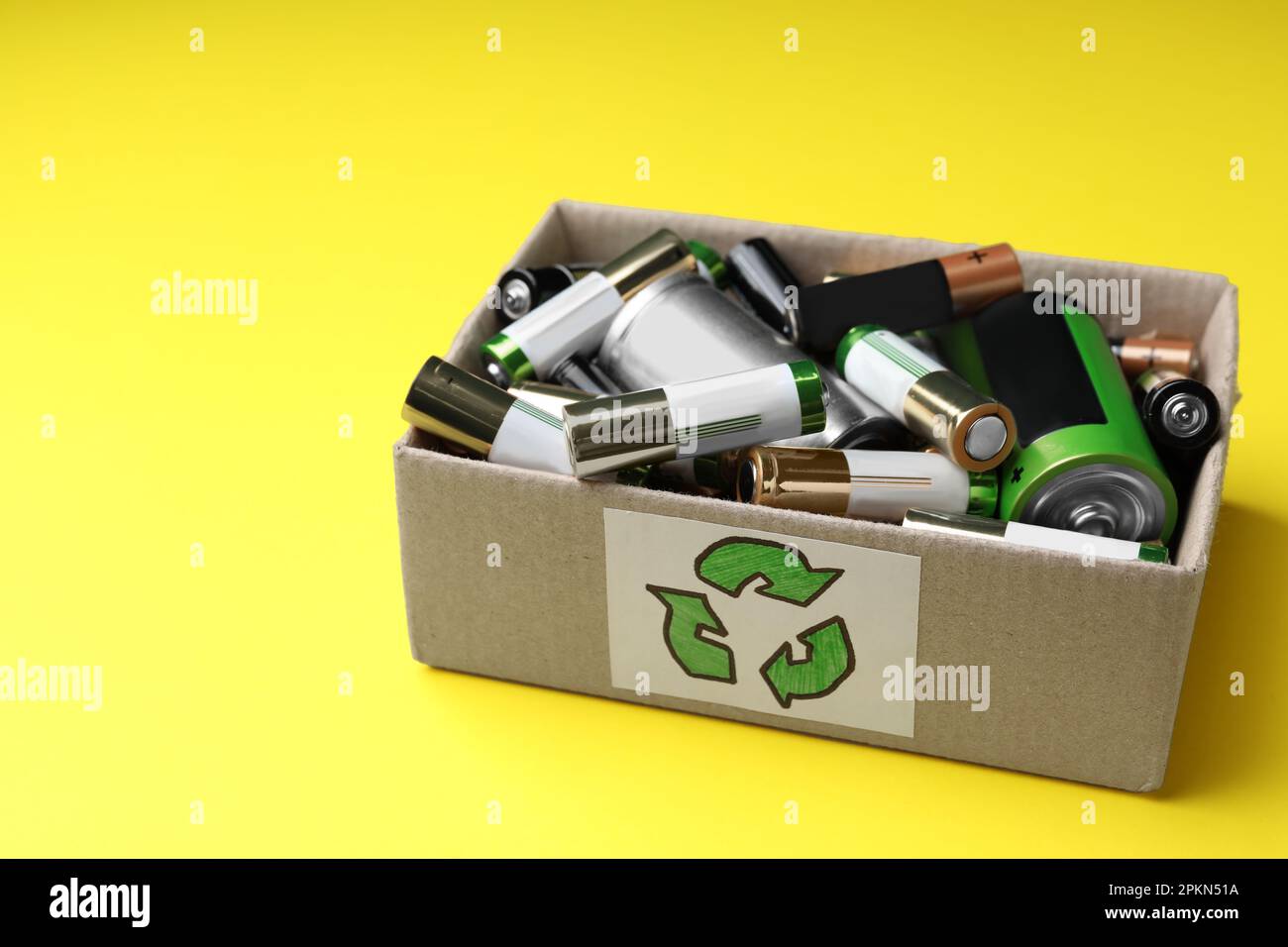 Used batteries in cardboard box with recycling symbol on yellow