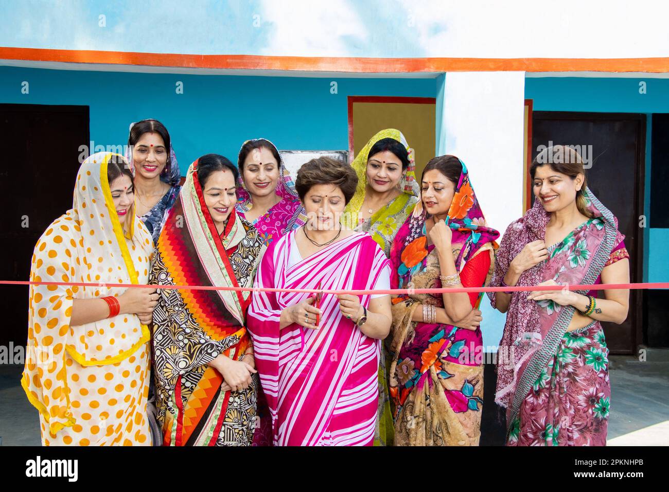 Indian business woman in sari cutting red ribbon while colleagues are clapping hands. Women empowerment. Stock Photo
