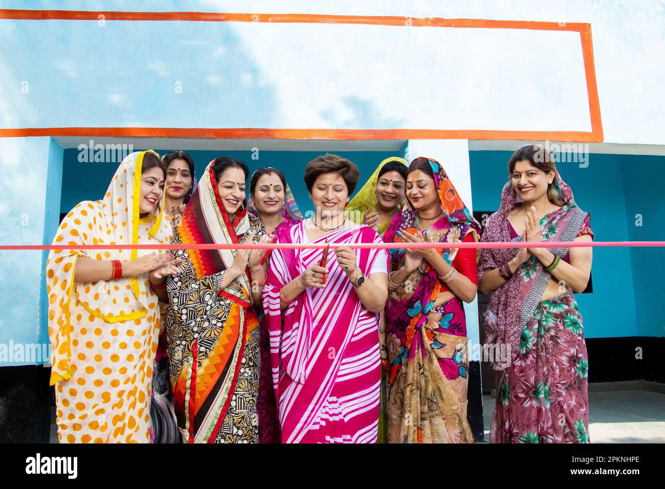 Indian woman in sari cutting red ribbon while colleagues are clapping hands. Women empowerment. Stock Photo