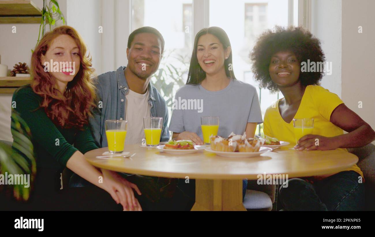 Multiethnic friends smiling at camera while eating breakfast at home Stock Photo