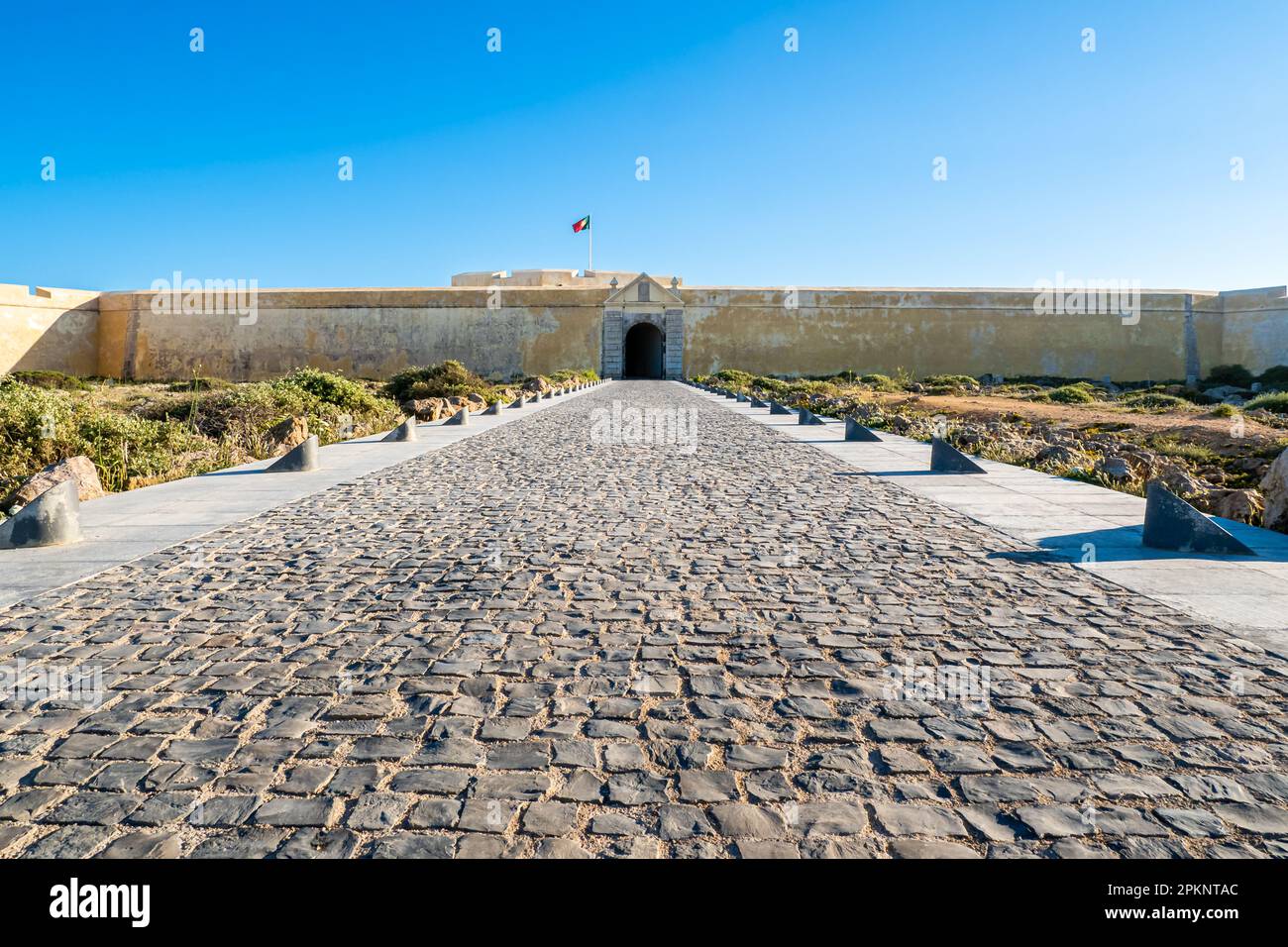Grand entrance of Fortaleza de Sagres, a historic fortress in the Algarve area of Portugal, is captured in a stunning front view, with a vast driveway Stock Photo