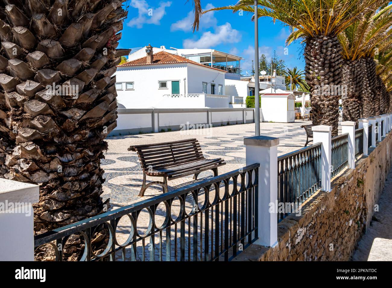 On a sunny day in May, the balustrade along the tranquil Av. Dos Pescadores promenade in the charming Algarve village of Luz overlooks Praia da Luz. Stock Photo