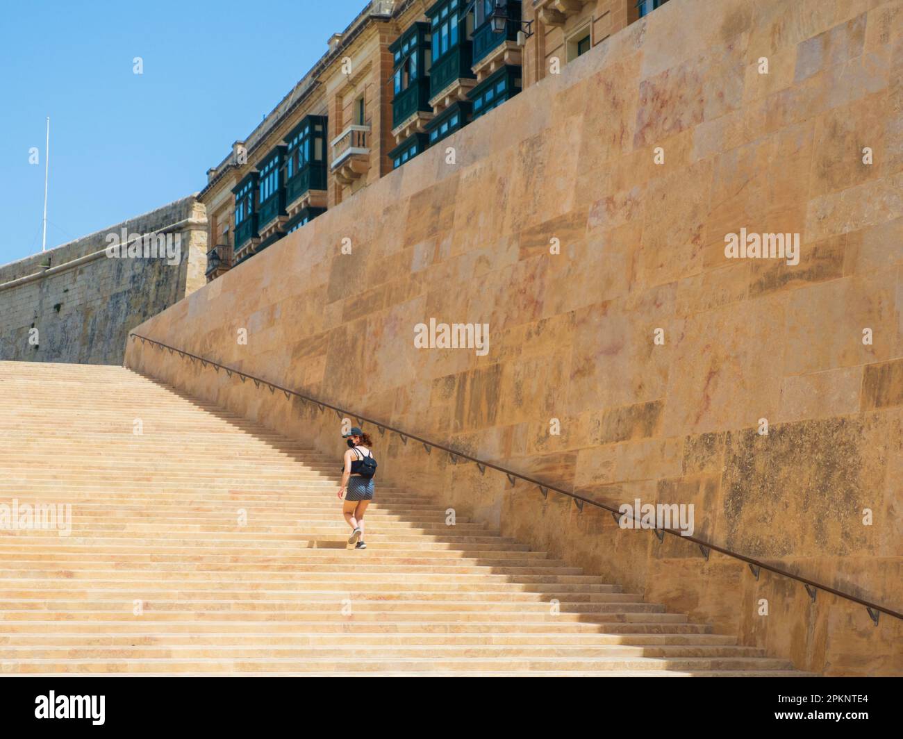 Valletta, Malta - May, 2021: Young woman climbs the huge stairs next to the city walls near the Valletta city gate. Europe Stock Photo