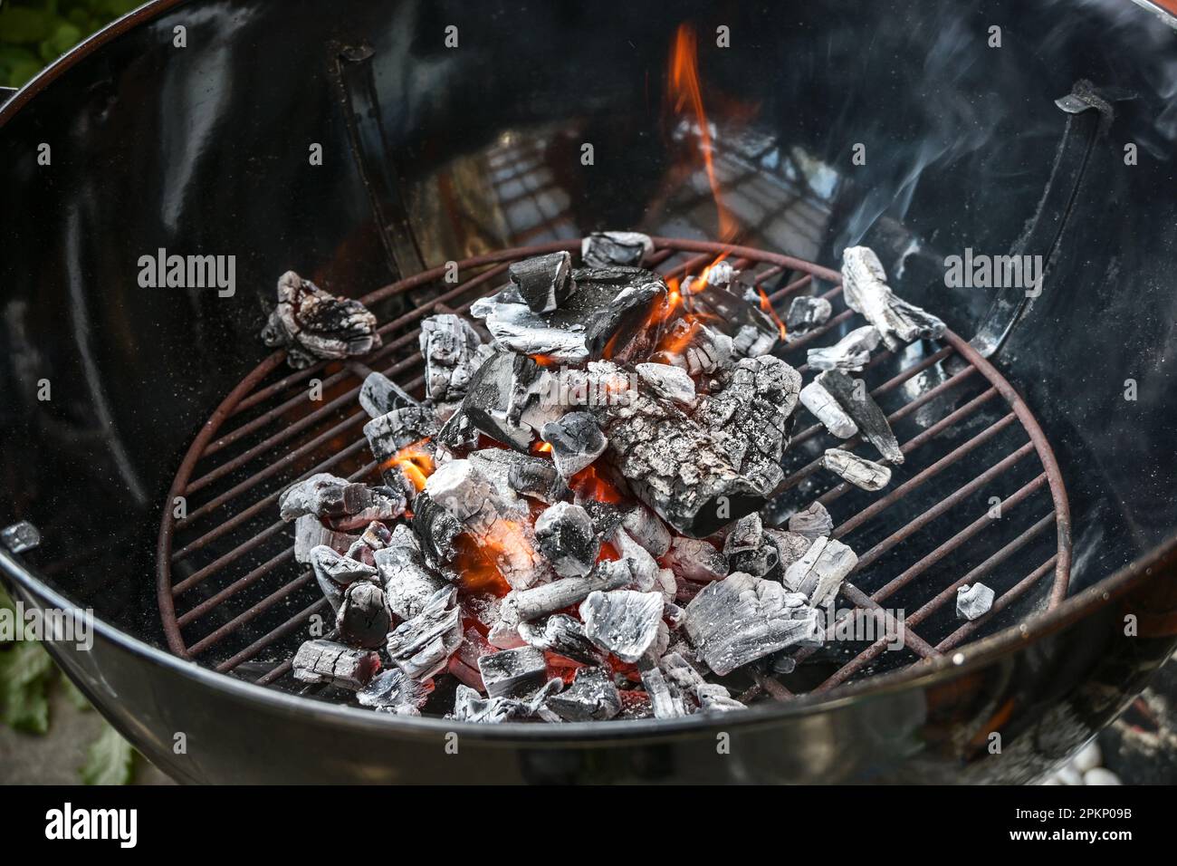 Mobile round grill with glowing charcoal, small flames and smoke, preparation for a barbecue