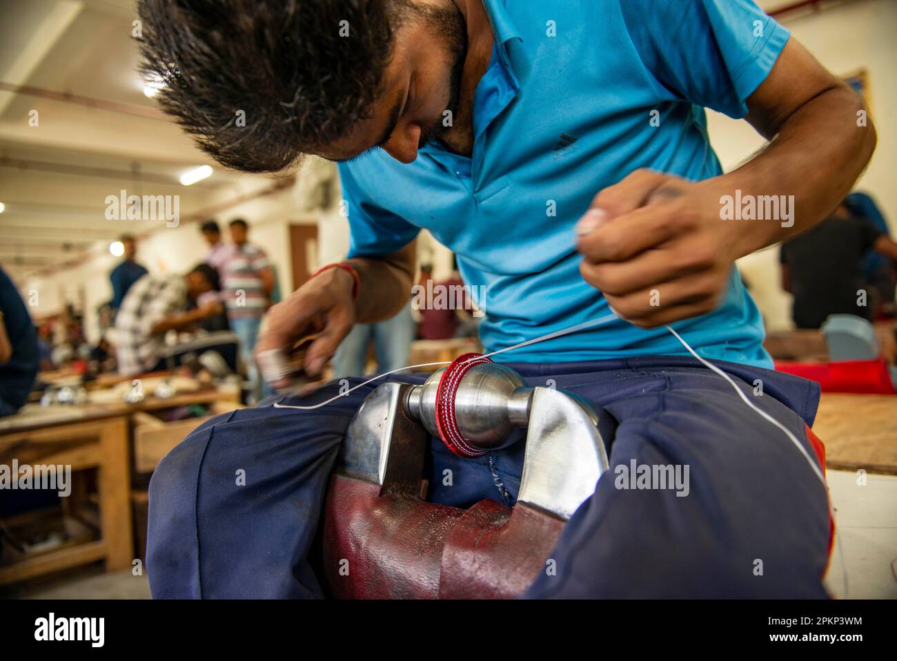 An employee stitches the leather seam for a cricket ball at the