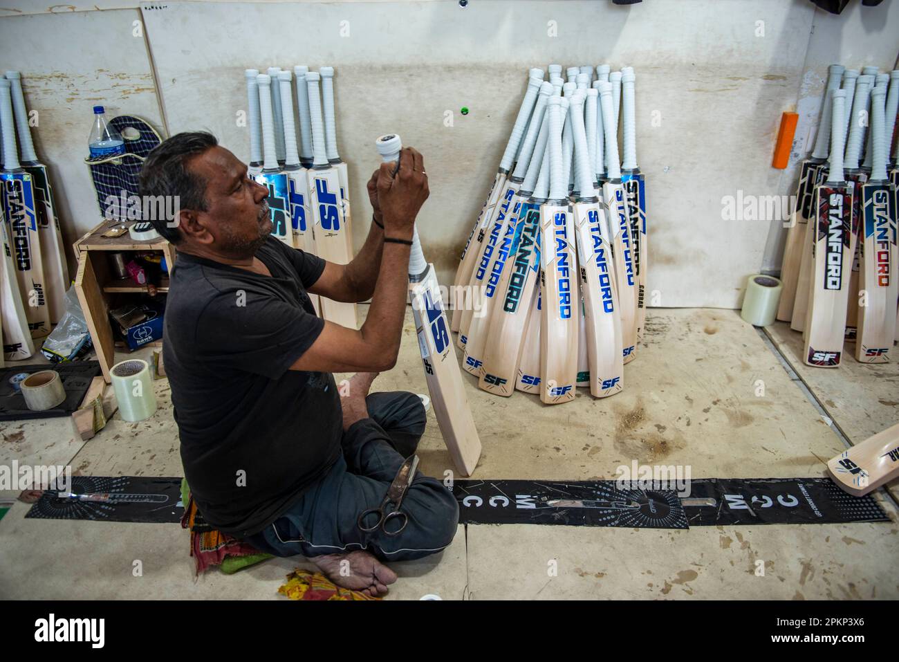 A worker applies rubber bat grip on cricket bat handle at the Stanford