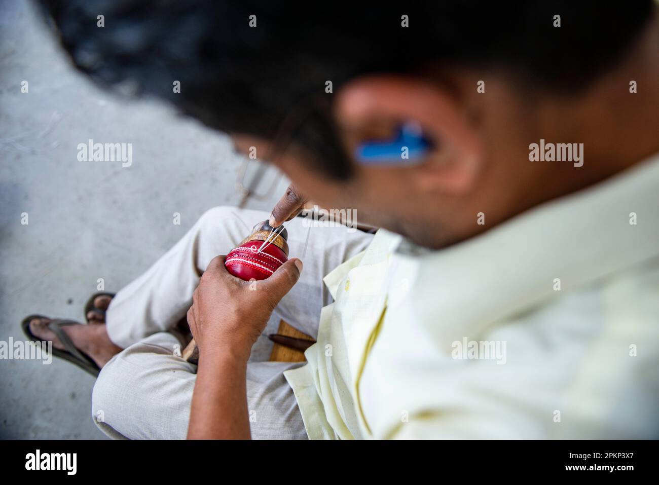 An employee stitches the leather seam for a cricket ball at the