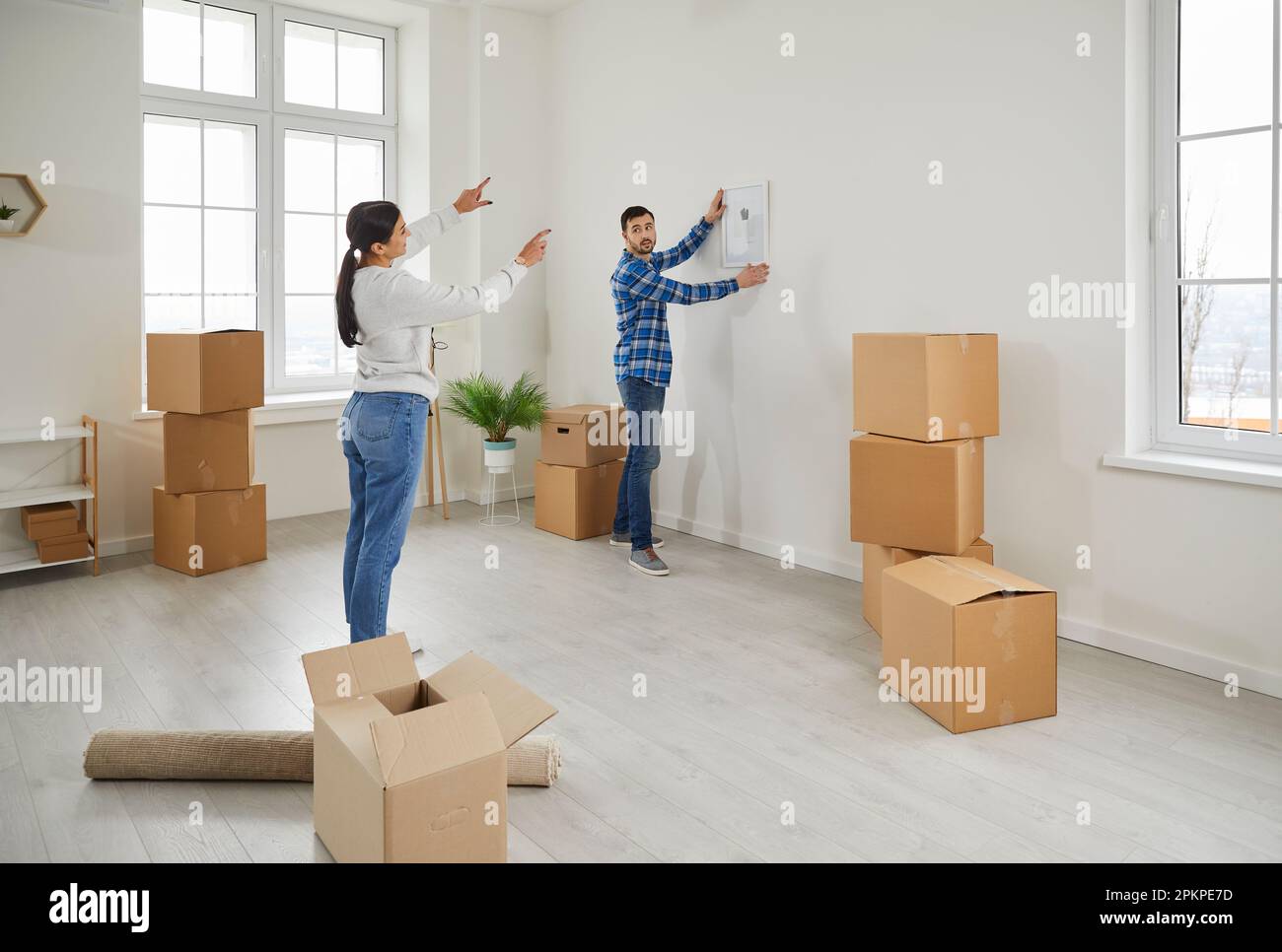 Young couple moving to new home and hanging photo or picture on wall in their new house. Stock Photo