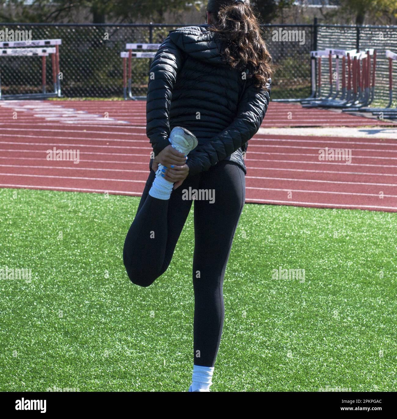 Rear view of a high school female is stretching her leg during track