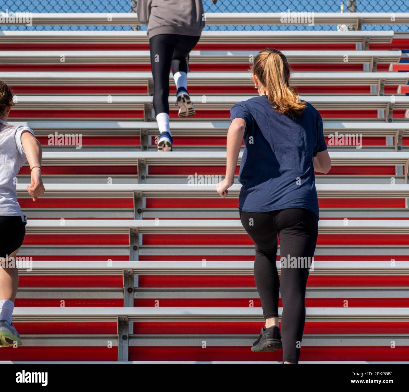 Rear view of three girls running up bleacher steps during an early