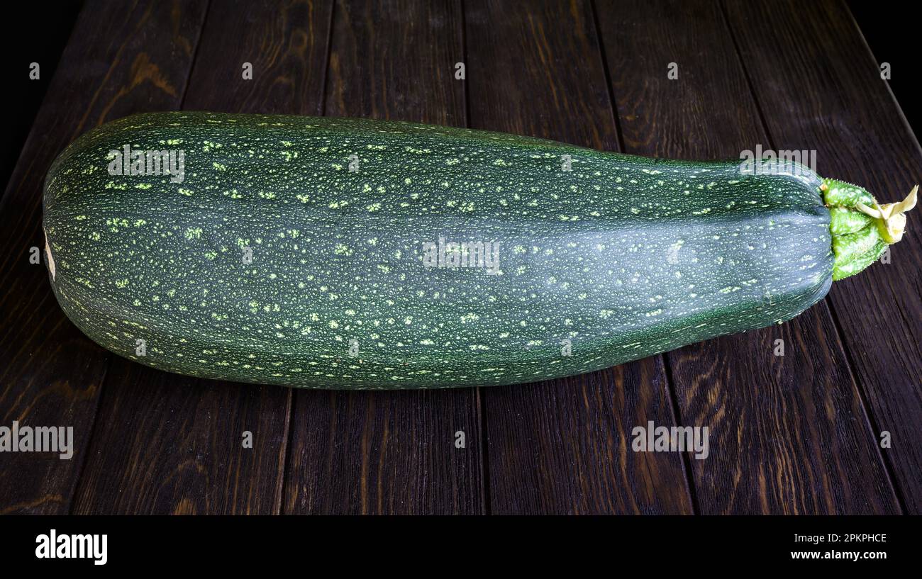Vegetable marrow zucchini on vintage wooden table. Photography of one big fresh squash isolated on dark planks. Theme of zucchini, organic food, natur Stock Photo