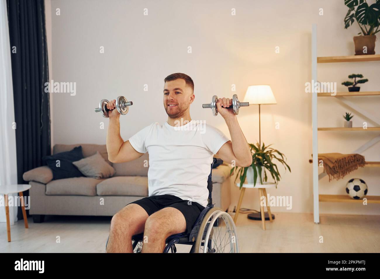 Doing exercises by using dumbbells. Disabled man in wheelchair is at ...