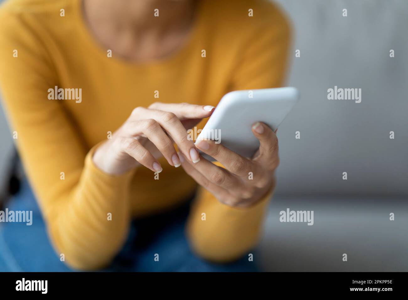 Unrecognizable Lady Using Modern Smartphone While Sitting On Couch At Home Stock Photo