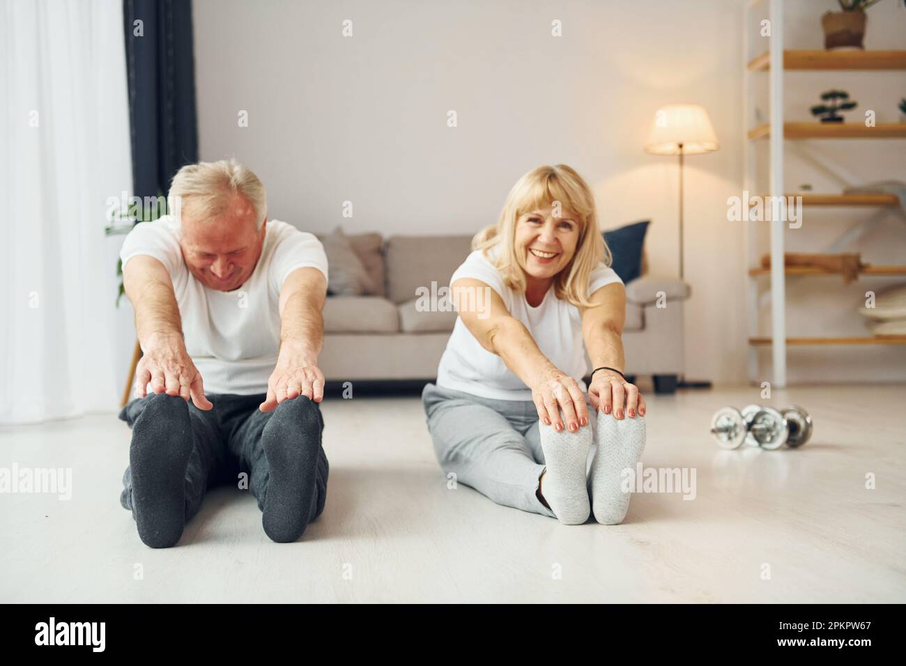 Sitting and doing exercises. Senior man and woman is together at home Stock Photo