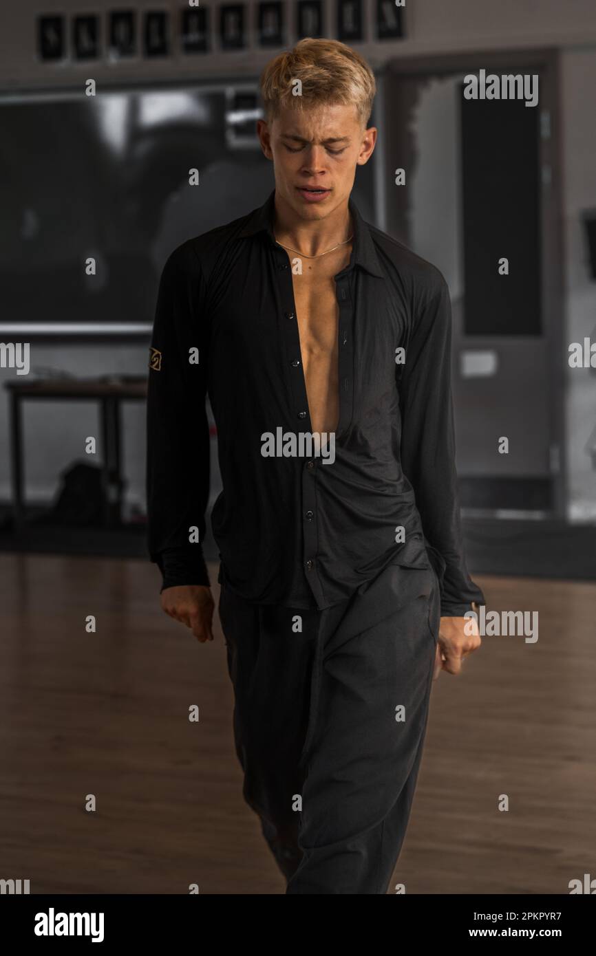 A male dancer standing in black clothes with an expression of pain on his face Stock Photo