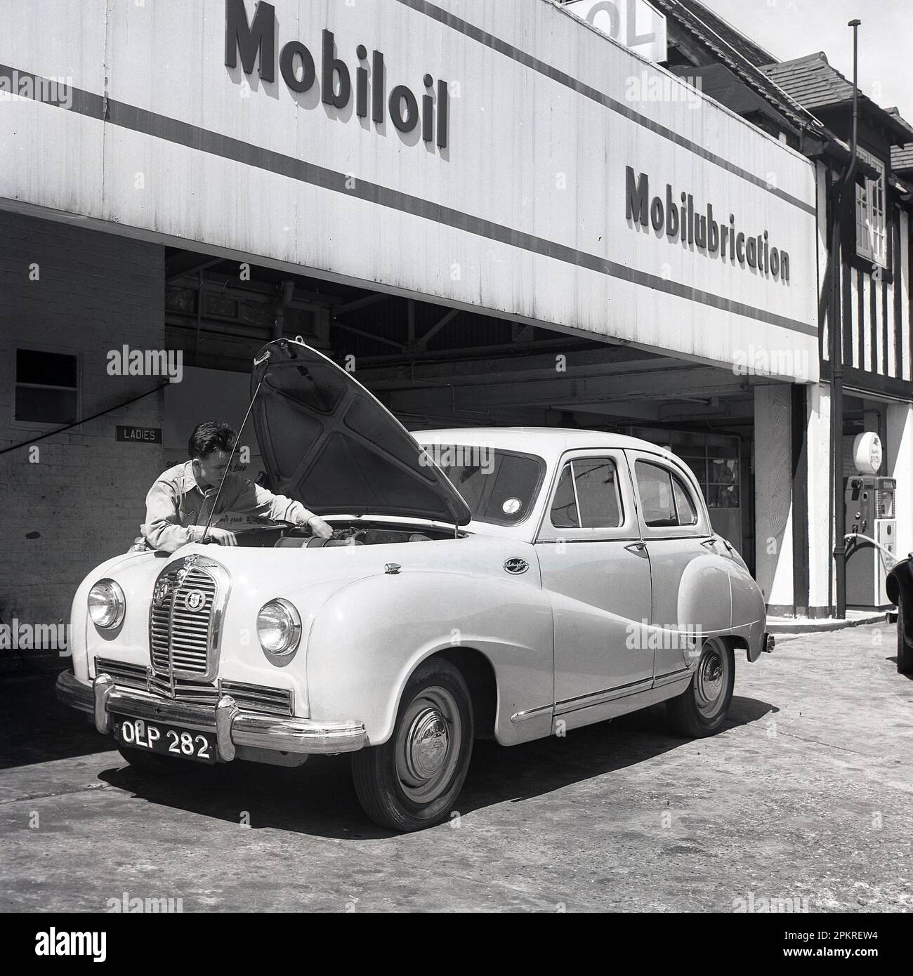 1950s, historical, a male service station attendant cleaning the front windscreen of a Austin motorcar, at the Ravenscroft Service Station, a new Mobilgas petriol and service station, London, England, UK. Sign on side of British-made car says Austin/England, Stock Photo