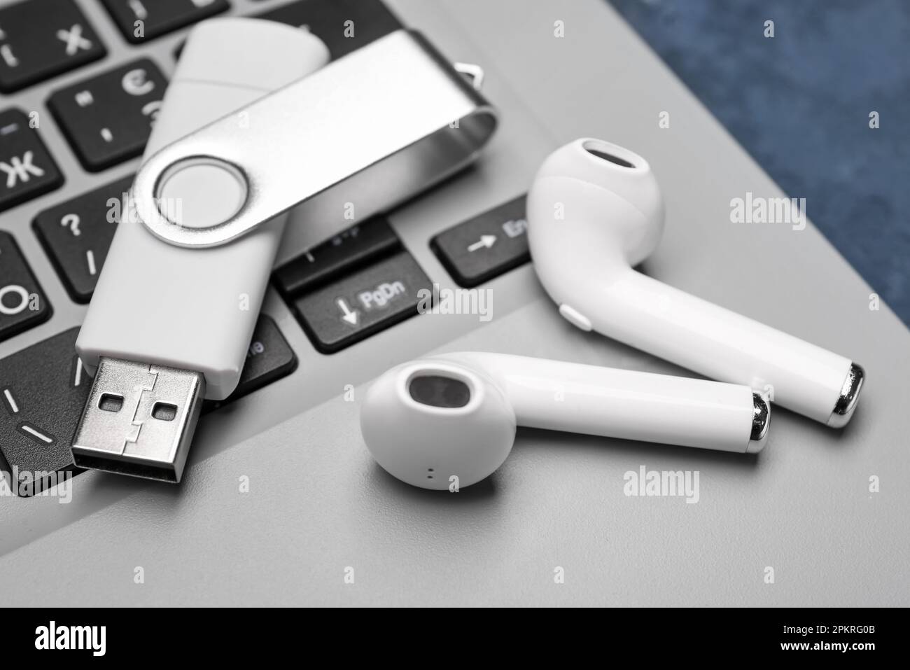 White USB flash drive and wireless earphones on modern laptop, closeup Stock Photo