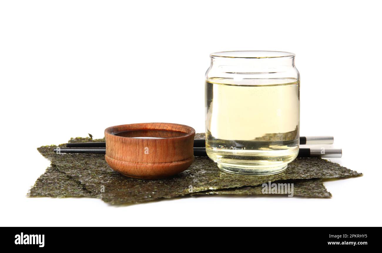 Glass of rice vinegar, soy sauce and nori sheets on white background