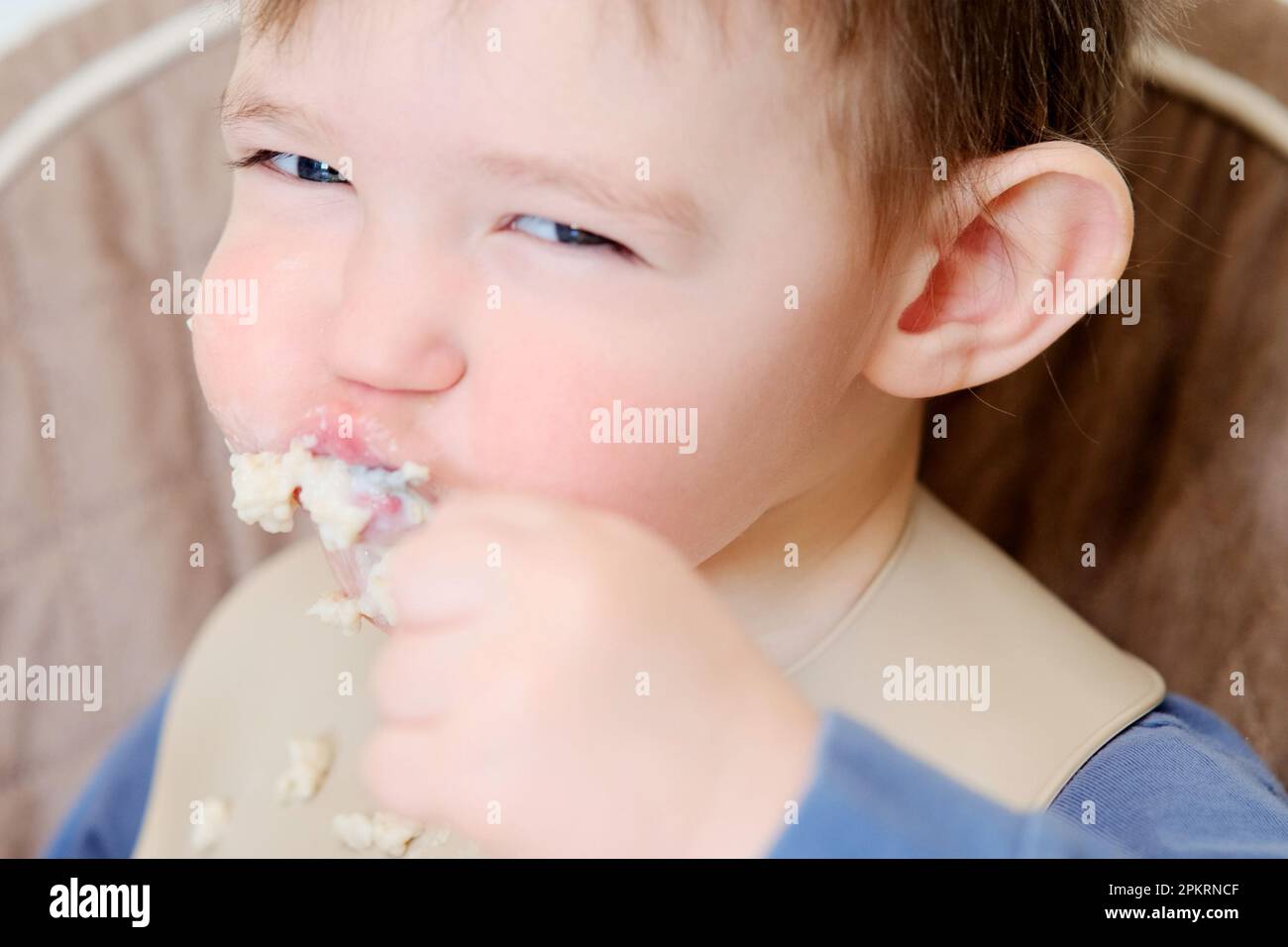 A happy child eats porridge with a spoon while sitting on a high chair