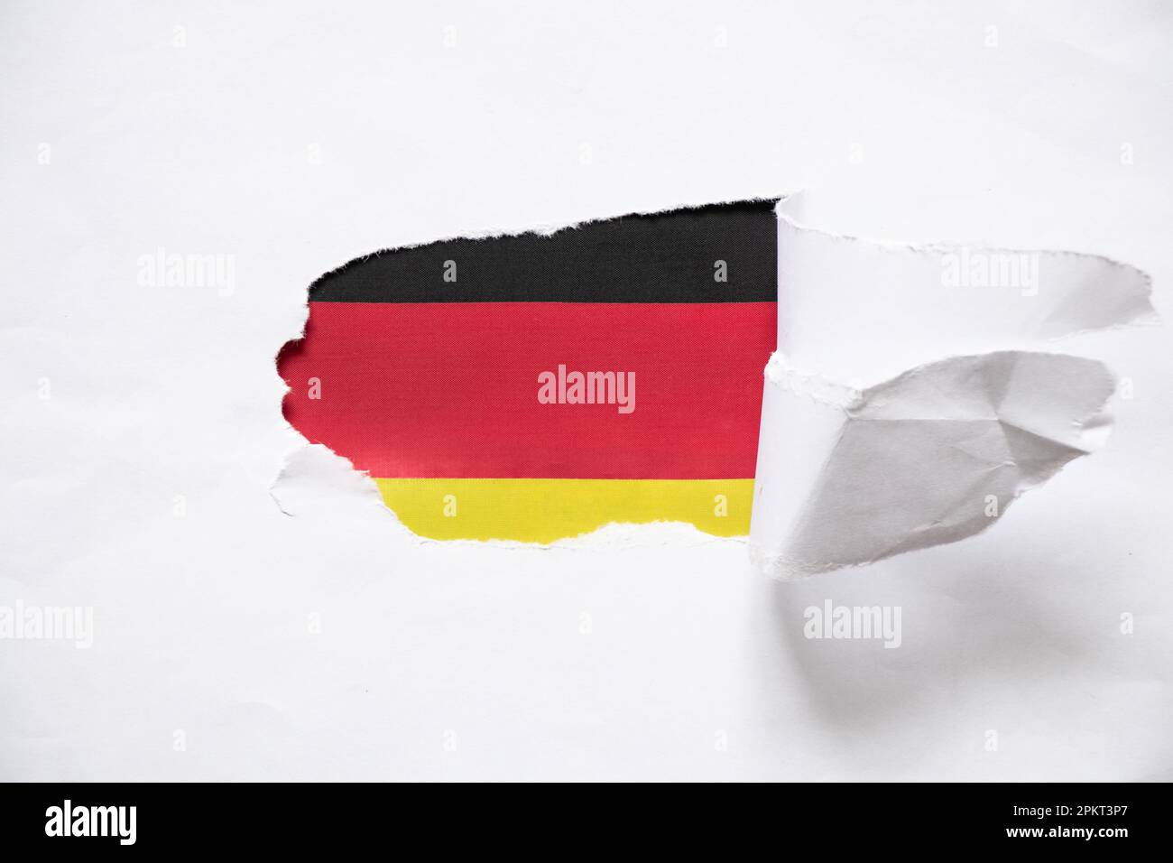 Torn white paper and the flag of Germany is visible in the hole as a background Stock Photo