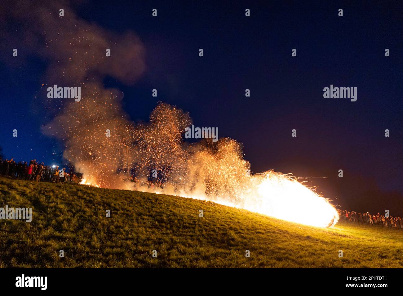 09 April 2023, North Rhine-Westphalia, Lügde: A burning Easter wheel rolls down the Osterberg towards the village of Lügde at the annual Osterräderlauf. The organizer, the Osterdechenverein Lügde, has been around for 100 years. In Lügde, Lippe, spectators were once again drawn to the Easter Wheel Run on Easter Sunday. As darkness falls, wooden wheels braided with straw and set on fire roll down a hillside into the valley. Photo: Christoph Reichwein/dpa Stock Photo